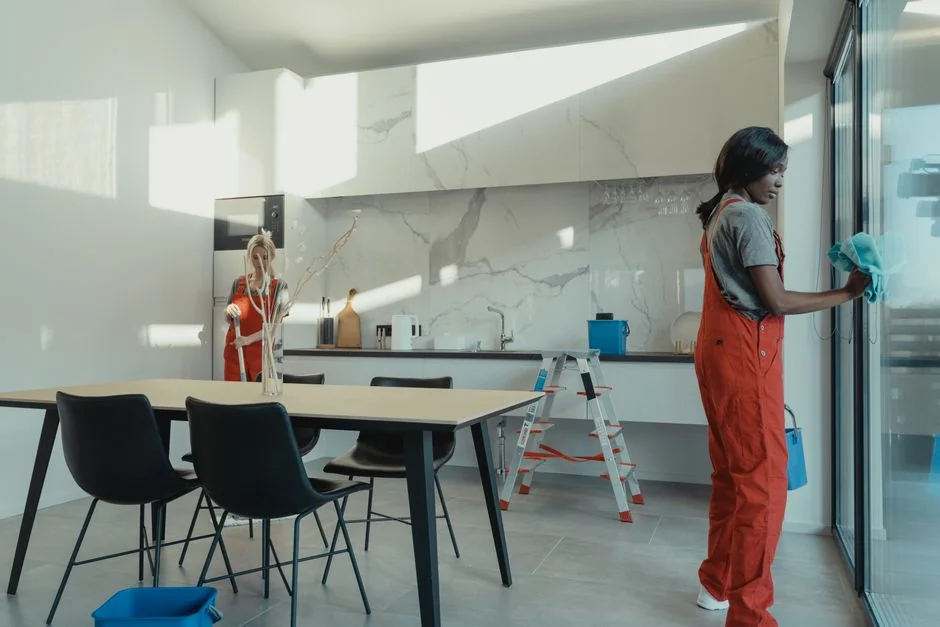 A man cleaning a glass door indoors using a spray bottle and cloth.